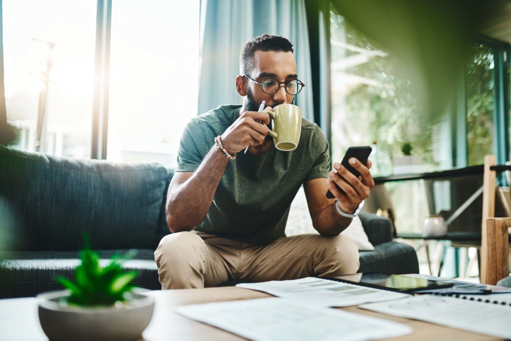 man sitting on couch using phone evoking cell phone stipend