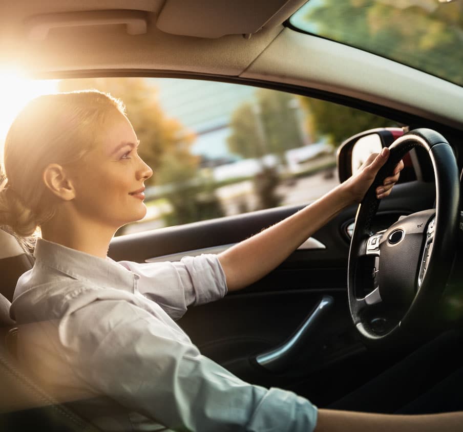 Woman sitting at the wheel of a car with her left hand on the steering wheel