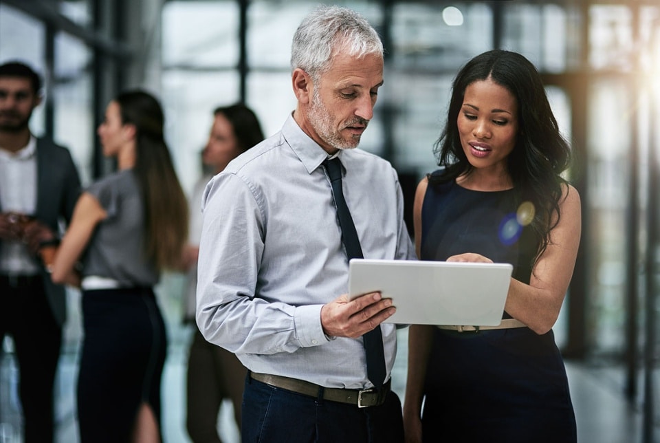A man and a woman looking at a white tablet with three people in the background