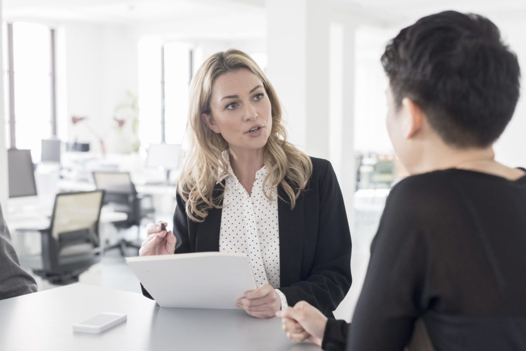 Woman holding papers and a pen talking to another person