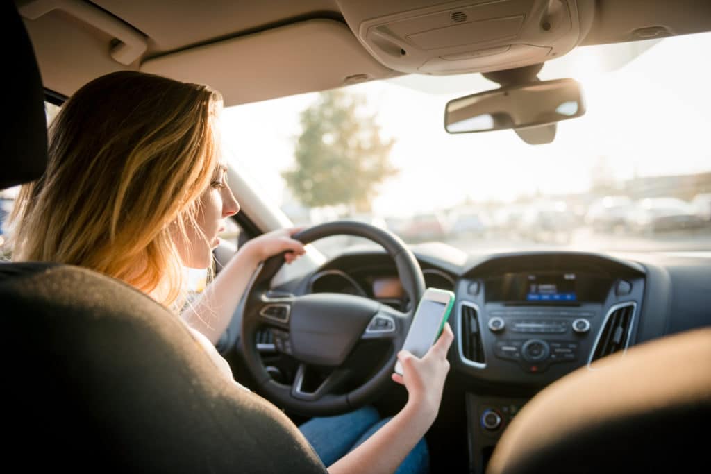 Woman sitting at the wheel of a car looking at a cell phone