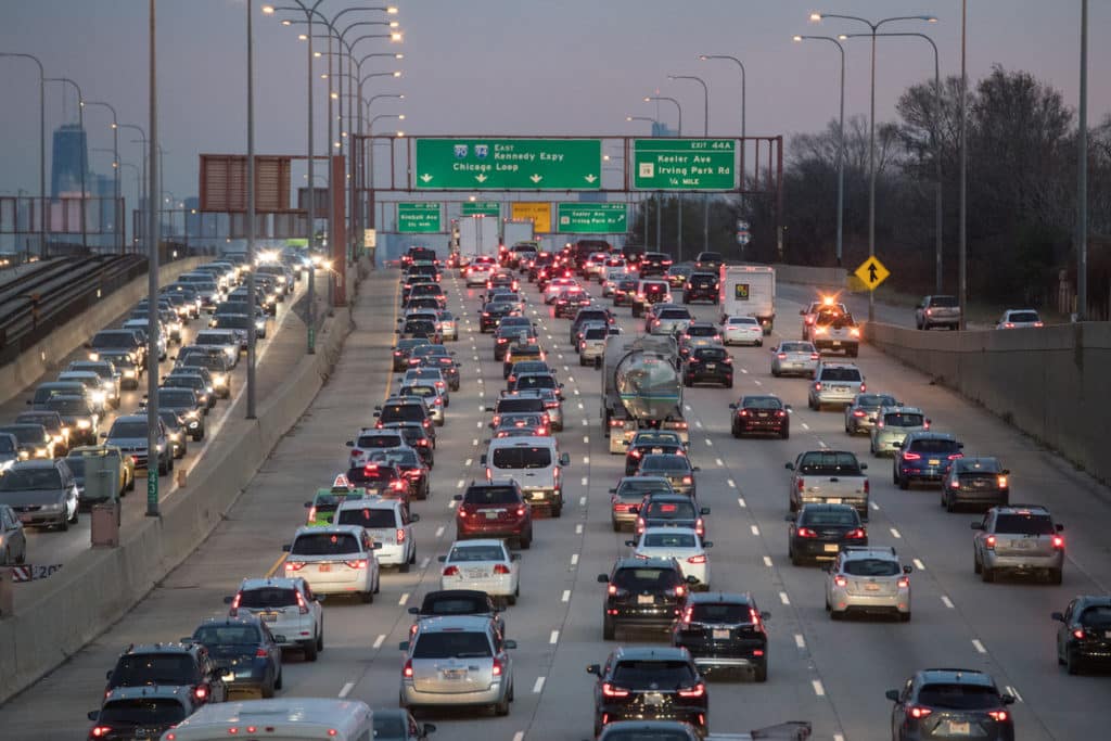 Many cars with headlights on driving on a freeway