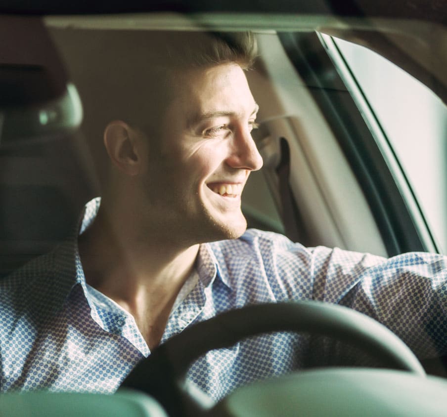 Man at the wheel of a car looking out the window and smiling