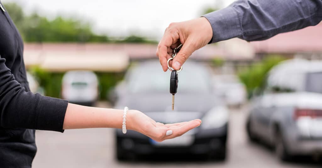 two people in a parking lot, one handing keys to the other, evoking "What to know when selling a car"