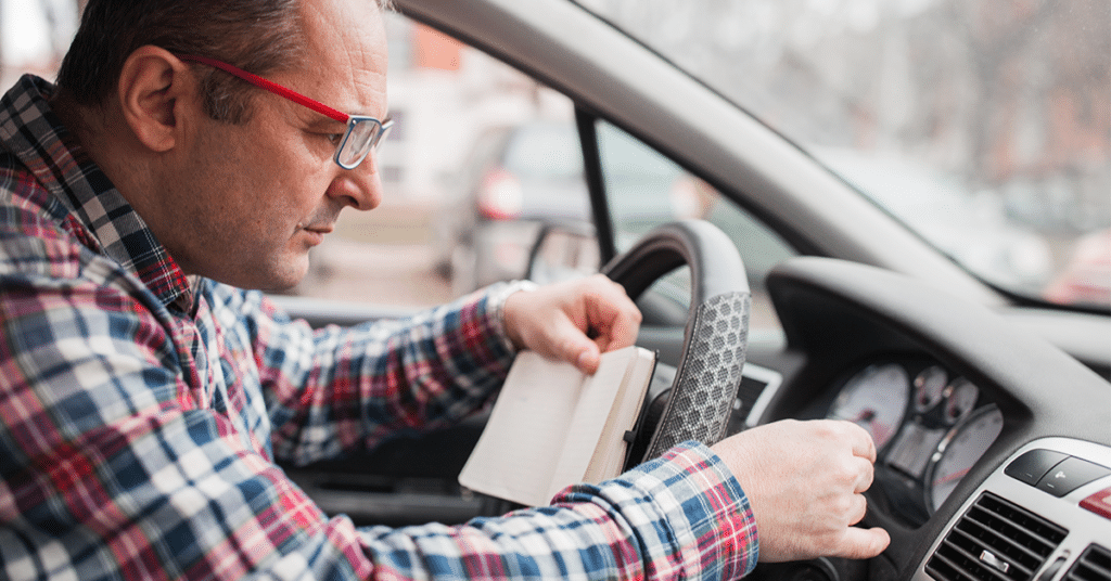 man in vehicle recording odometer, evoking manual mileage reporting