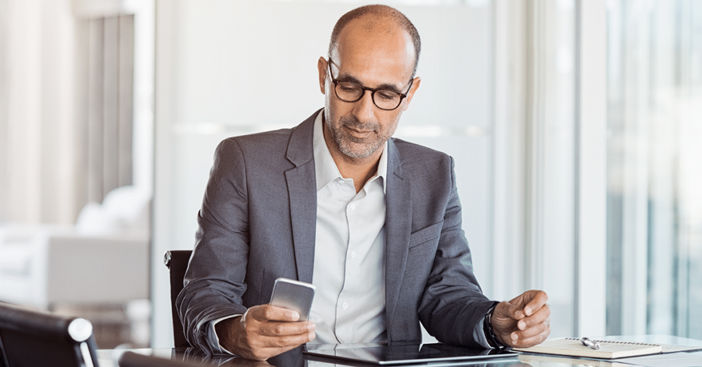 business man at a desk looking at his phone, evoking cell phone reimbursement