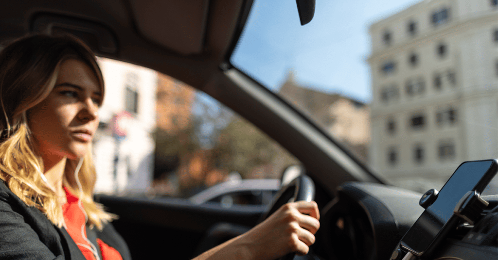 Woman sitting at the wheel of a car and a cell phone mounted to the dashboard